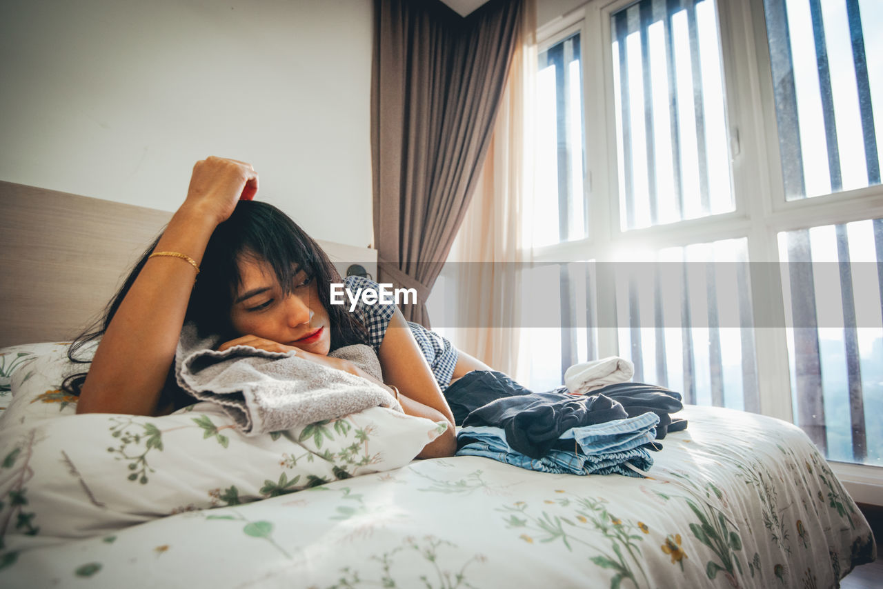 Tired young woman lying on bed at home