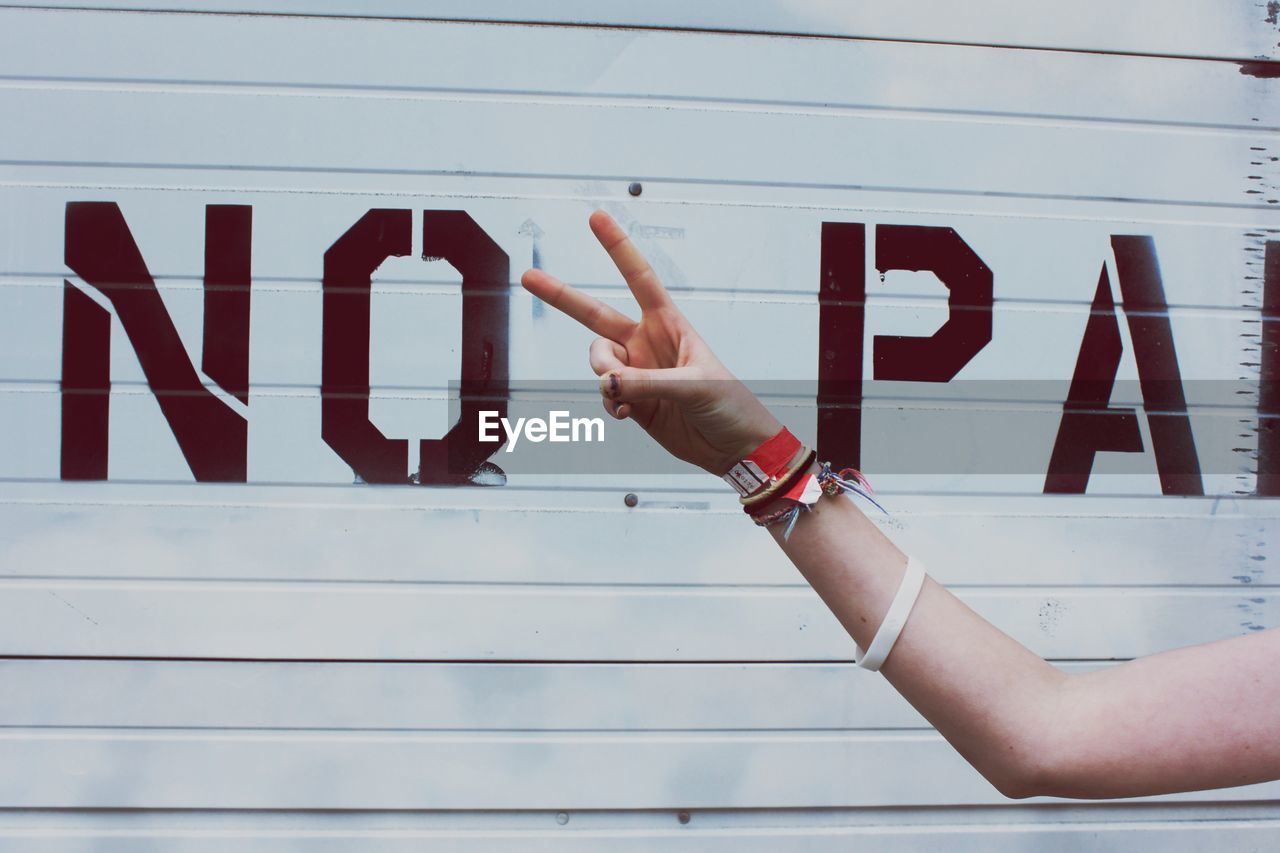 Cropped hand of woman gesturing peace sign against shutter