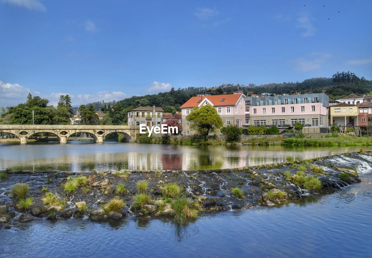 Arch bridge over river by buildings against sky