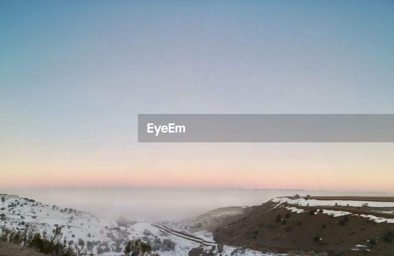 SCENIC VIEW OF SNOW COVERED MOUNTAINS AGAINST CLEAR SKY DURING SUNSET