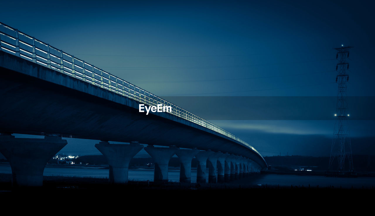 LOW ANGLE VIEW OF ILLUMINATED BRIDGE AT NIGHT