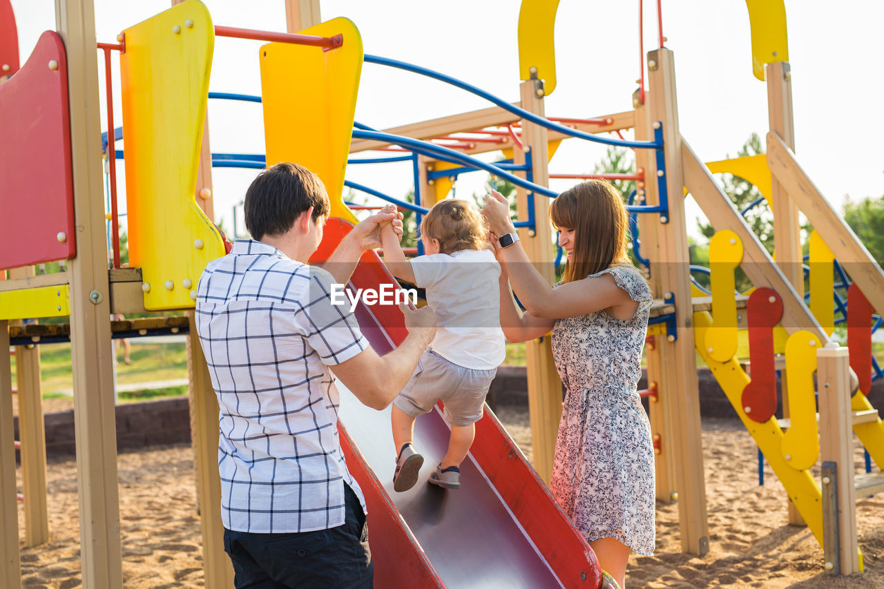 REAR VIEW OF PEOPLE ENJOYING IN PLAYGROUND