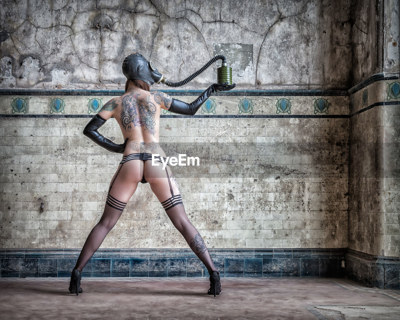 Full length of sensuous naked woman wearing gas mask while standing against wall