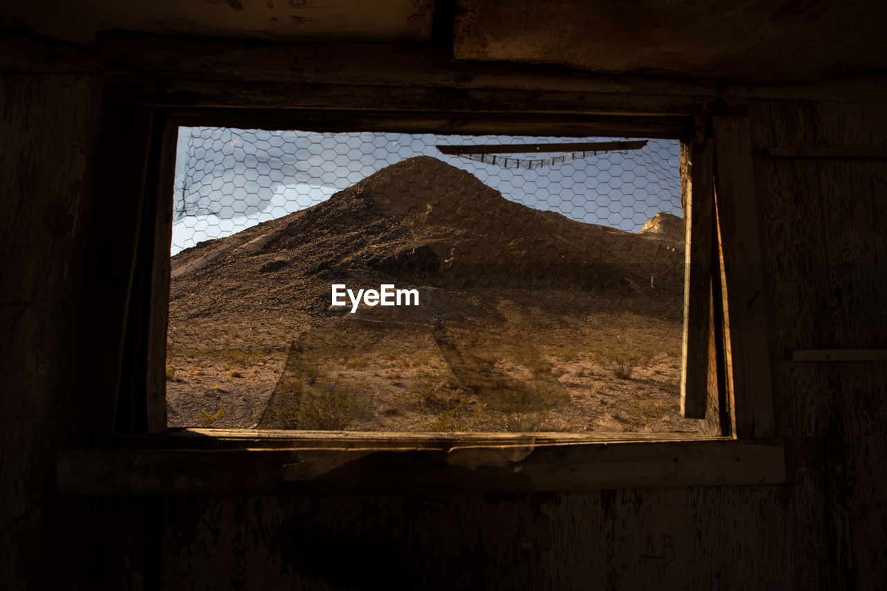 View of hill in desert landscape thru abandoned building window of ghost town 