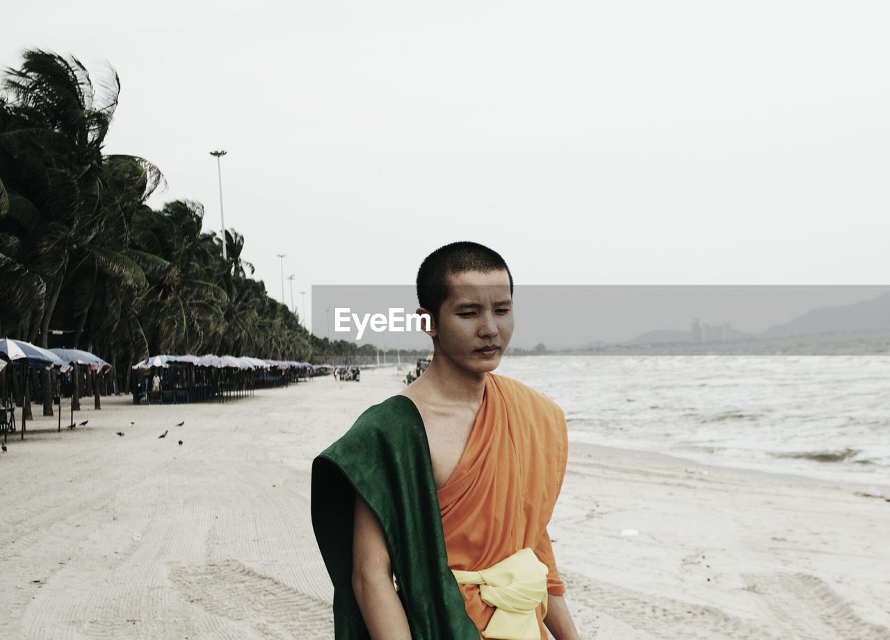 Monk standing at beach against clear sky