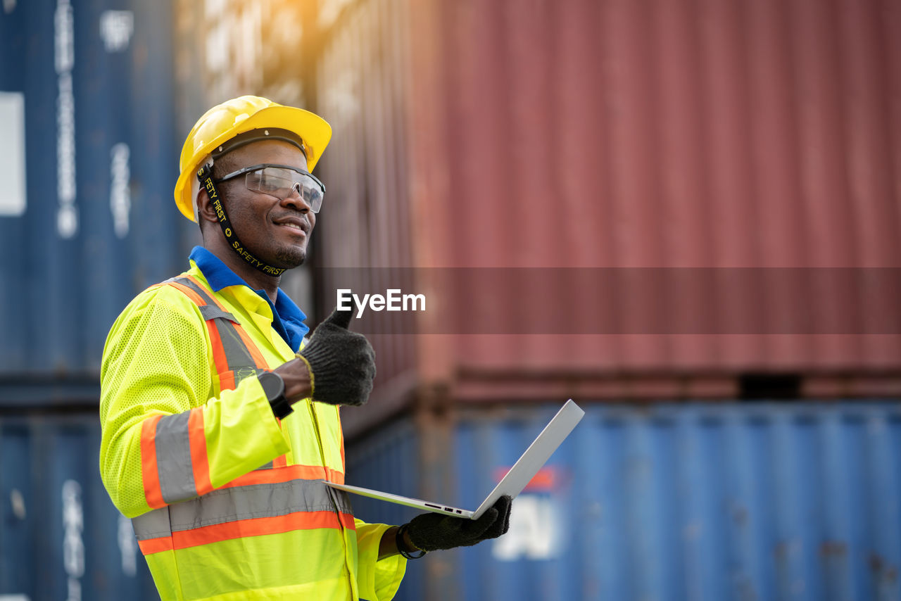 Worker holding laptop showing thumbs up while standing at dock