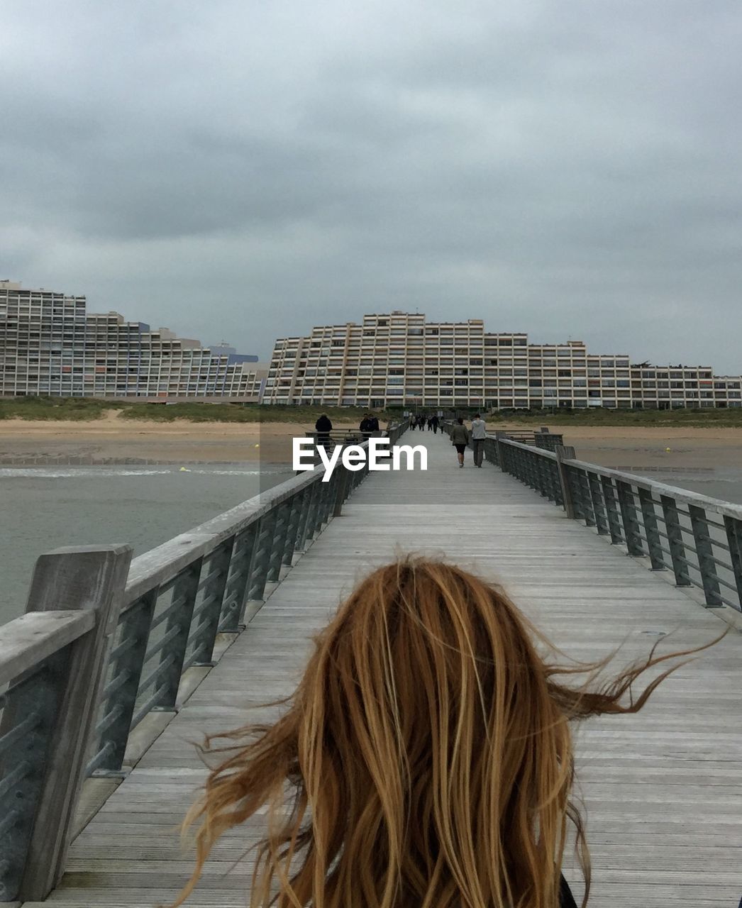 Rear view of woman on pier against cloudy sky