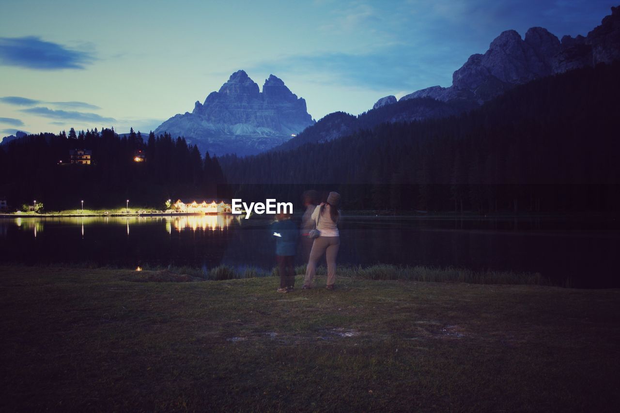 WOMAN STANDING BY LAKE AGAINST SKY DURING SUNRISE