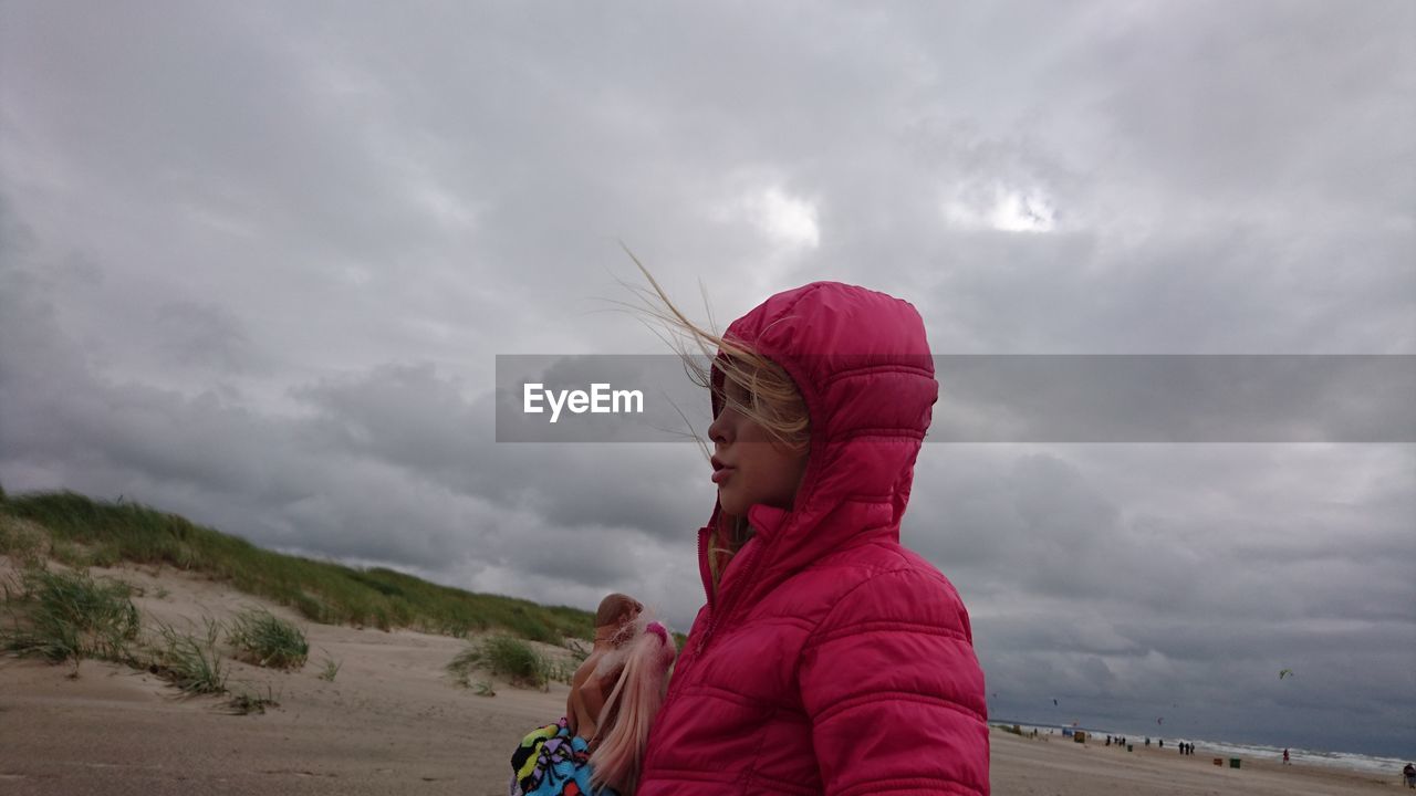 Side view of girl standing against storm clouds