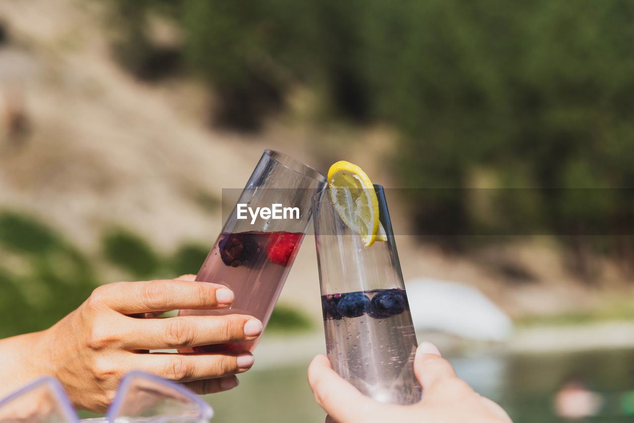 Two glasses touching for a cheers near an outdoor natural pool or hot spring.