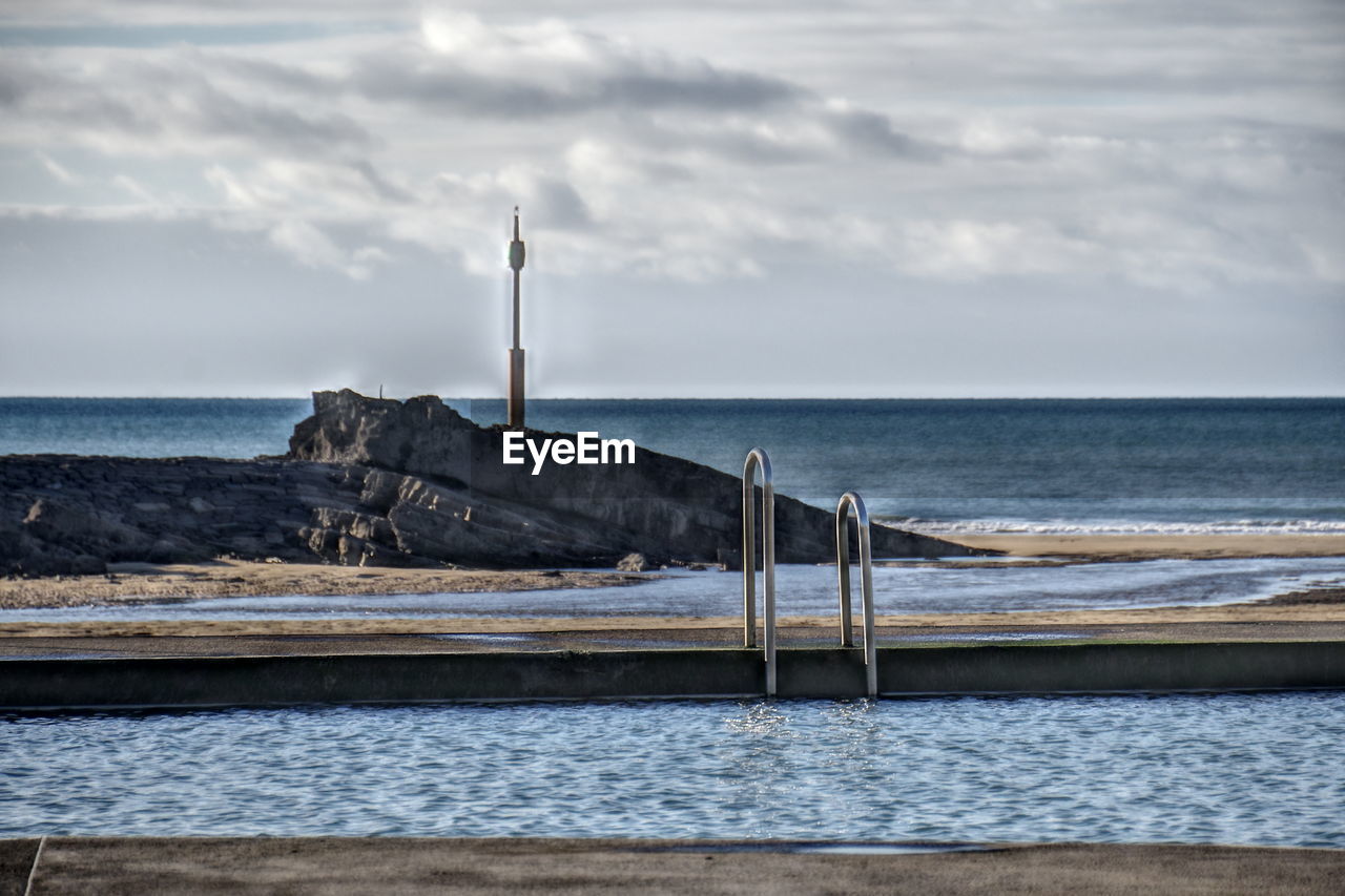 sea, water, ocean, sky, shore, coast, beach, land, cloud, tower, breakwater, wave, nature, horizon, scenics - nature, lighthouse, horizon over water, beauty in nature, architecture, no people, built structure, tranquil scene, tranquility, guidance, day, outdoors, sand, travel destinations, environment, pier, bay, coastline, travel, non-urban scene, idyllic, protection, security