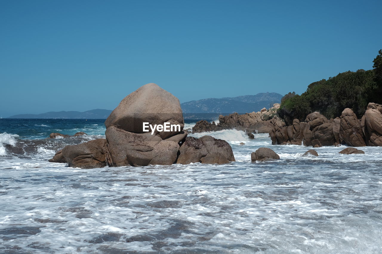 Rocks in sea against clear blue sky