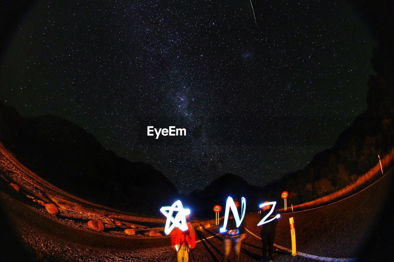 People holding illuminated alphabets against starry sky
