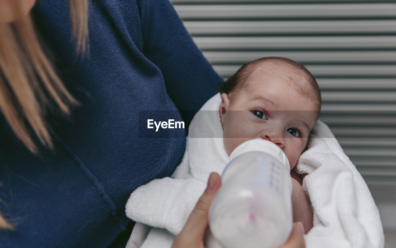 Midsection of mother feeding son with milk bottle