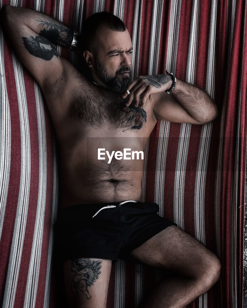 adult, one person, men, muscular build, indoors, strength, facial hair, beard, young adult, portrait, arm, lifestyles, macho, limb, striped, clothing, person, relaxation, waist up, curtain, tattoo, human leg, semi-dress, chest hair, studio shot