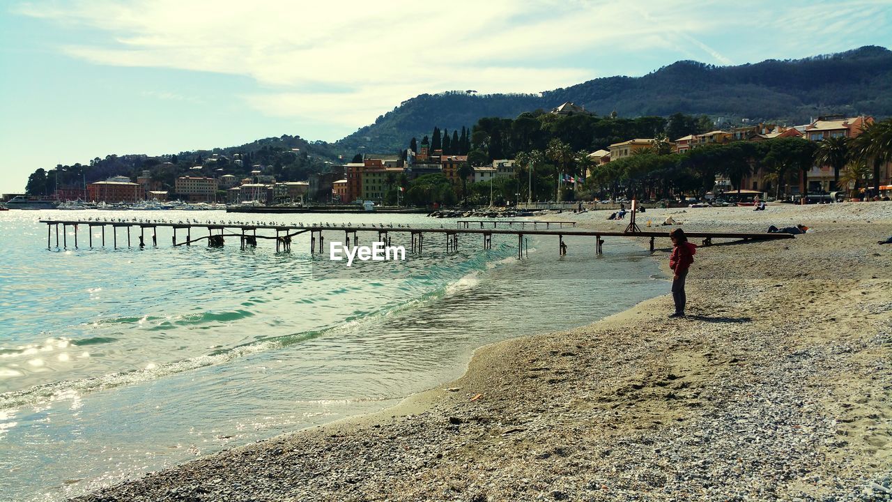 Boy standing at beach by mountains against sky