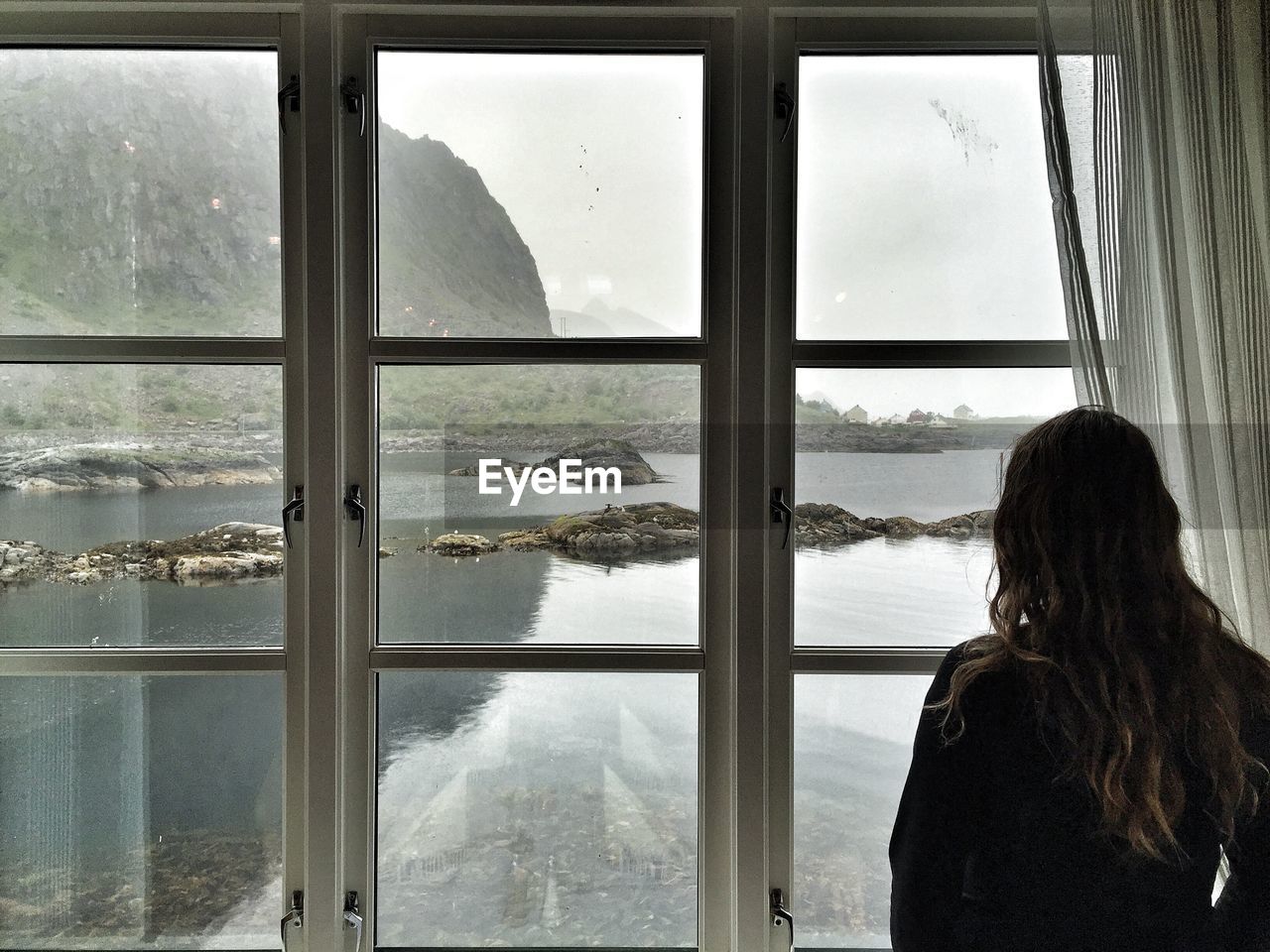 Rear view of woman looking river and mountain through window