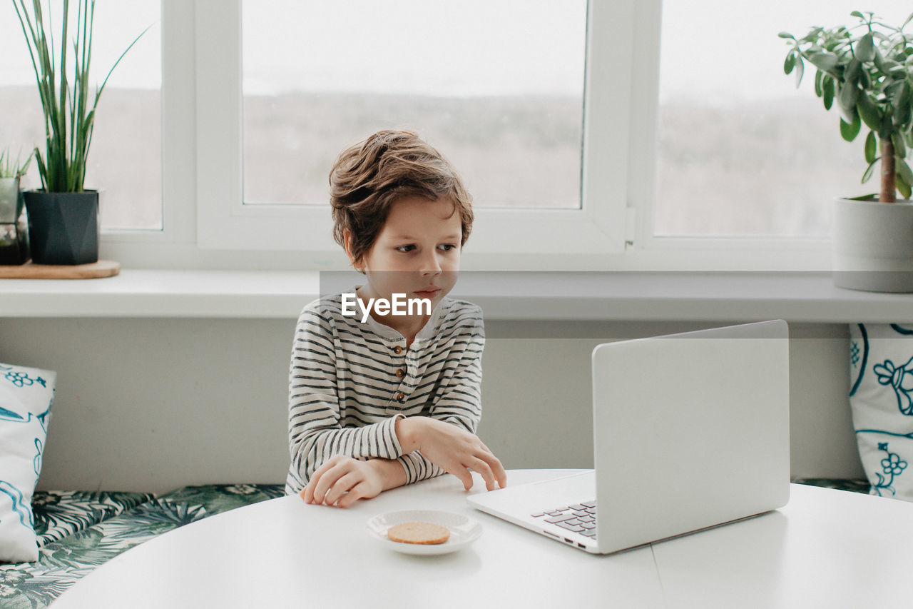 Little boy siting at the kitchen and look at the laptop. high quality photo