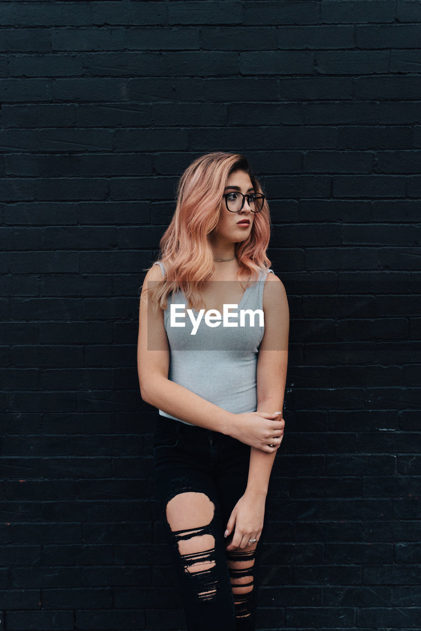 Young woman looking away while leaning on wall