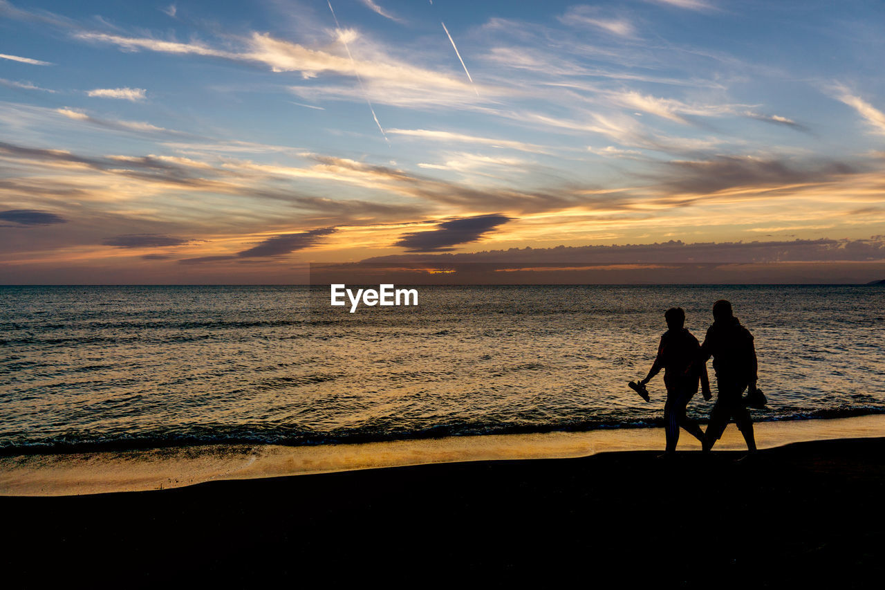 Silhouette people walking at shore on beach during sunset