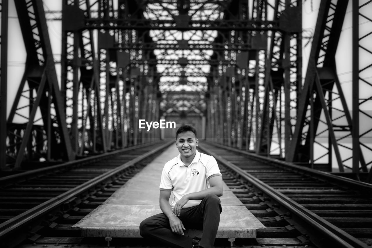 Portrait of man sitting on railway bridge