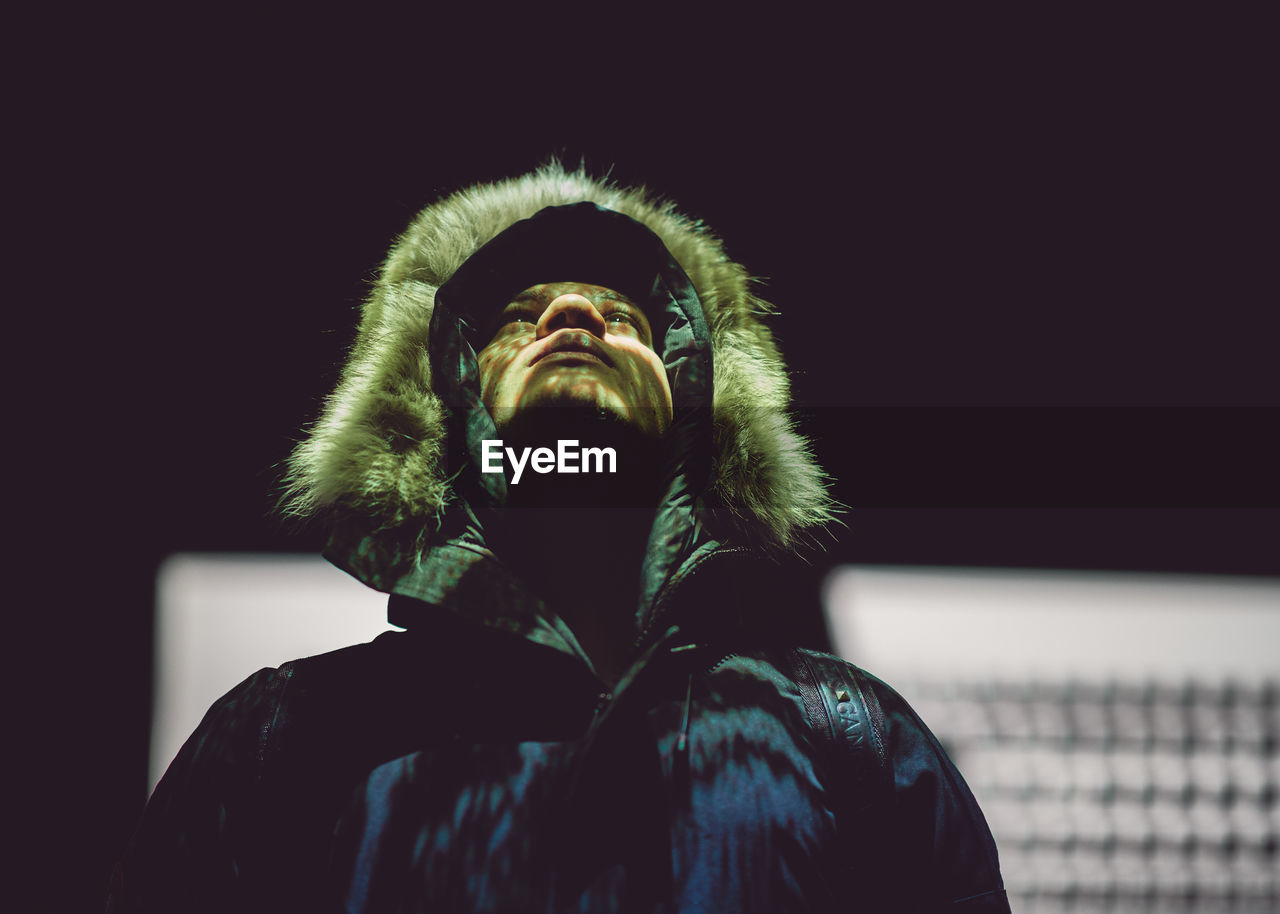 Man in fur coat looking up against wall