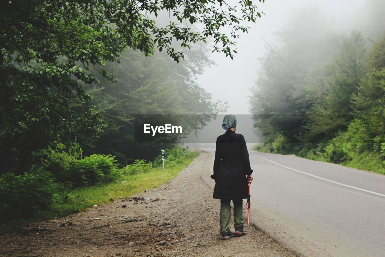 Rear view of woman standing on footpath by road in foggy weather