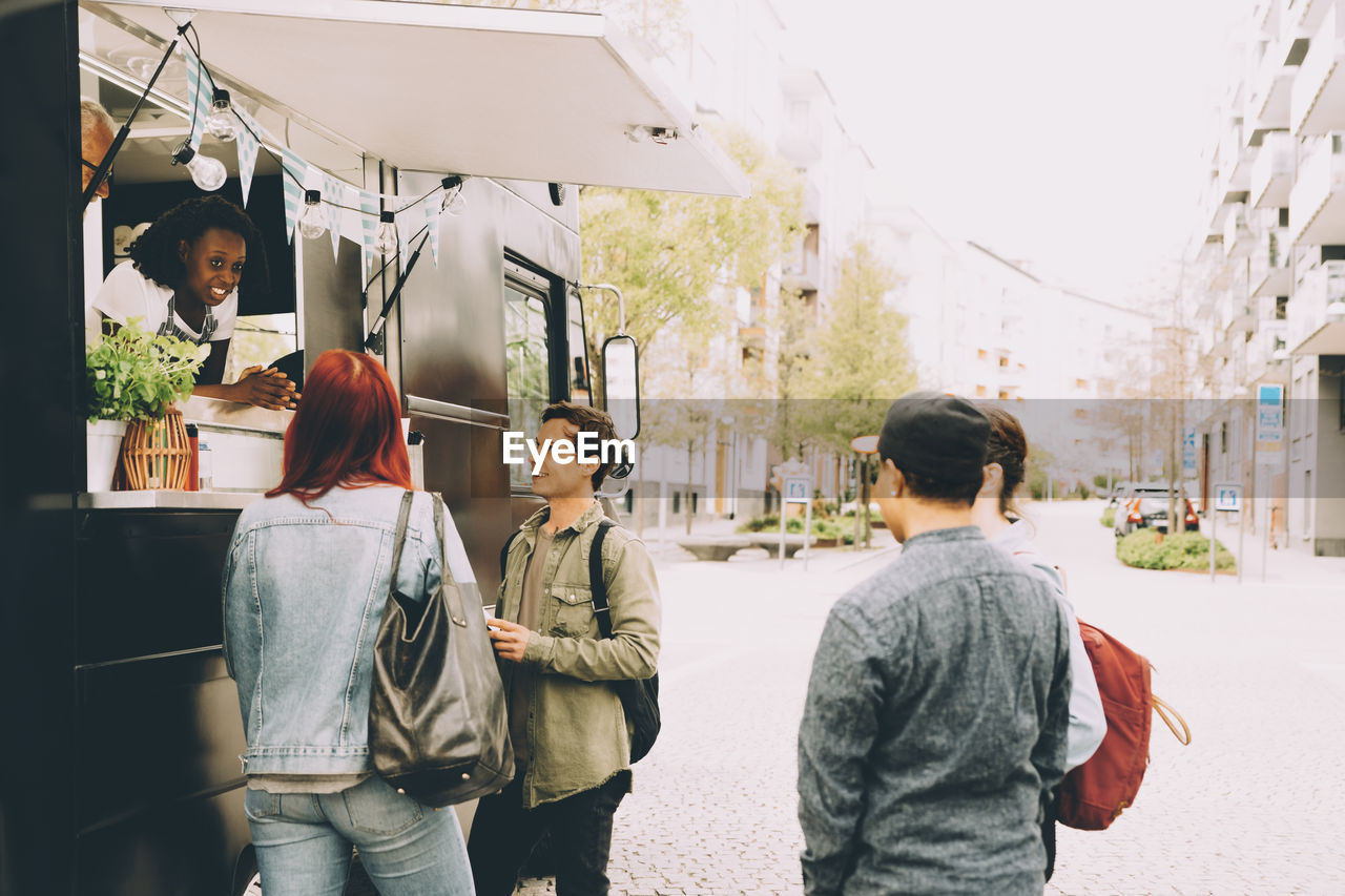 Owner with assistant talking to smiling customers by food truck on street