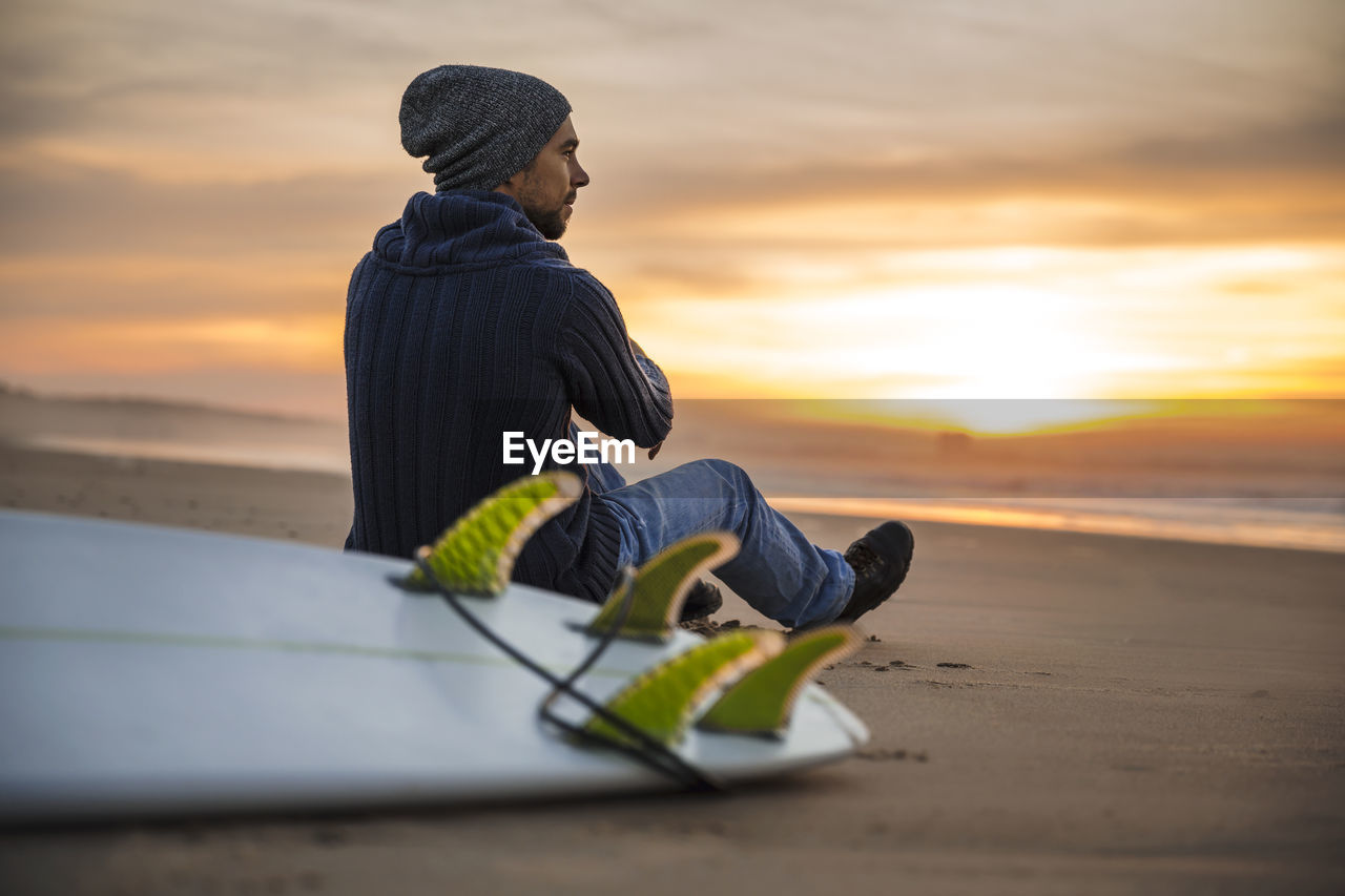 Man wearing sunglasses on beach against sky during sunset