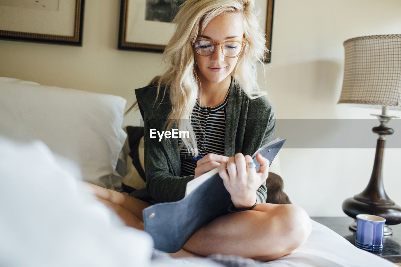 Woman writing diary while sitting on bed at home