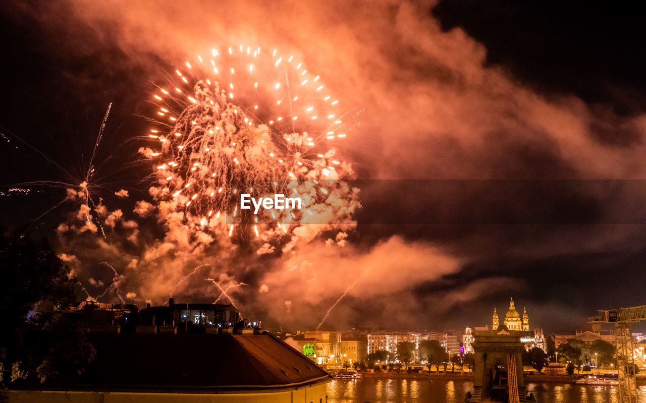 Firework display over illuminated city against sky at night