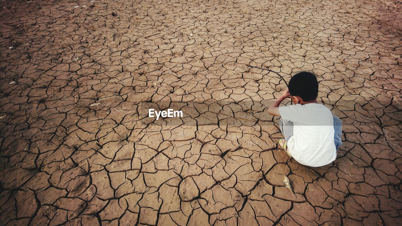 Rear view of boy crouching on cracked field