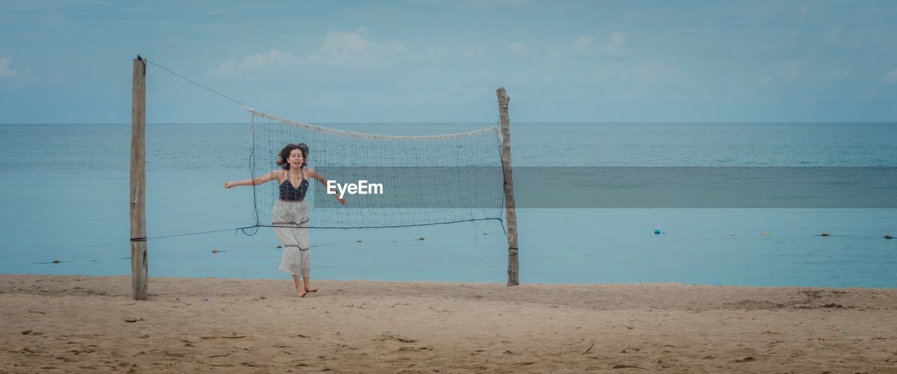 Woman jumping at beach seen through volleyball net