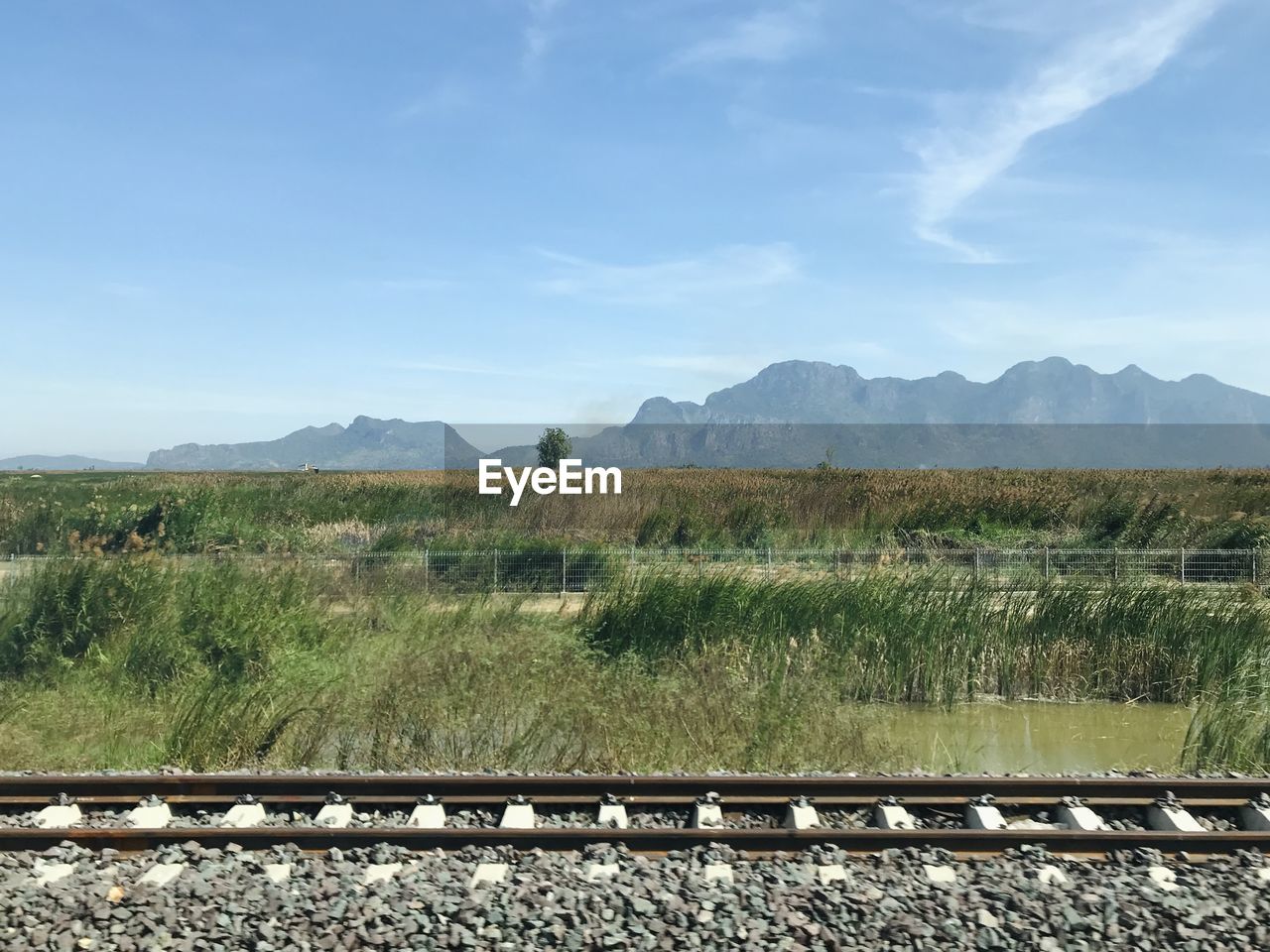 RAILROAD TRACKS BY FIELD AGAINST SKY