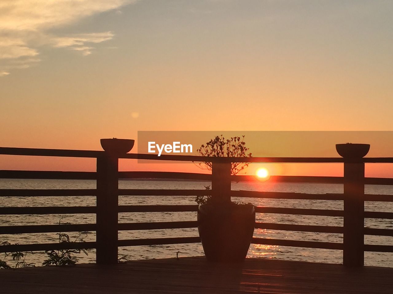 Silhouette railing by sea against sky during sunset