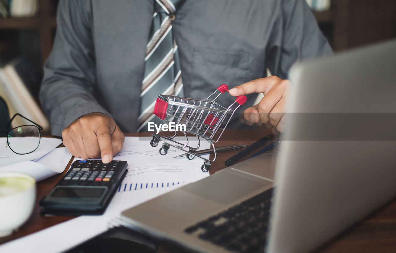 Midsection of businessman calculating at desk in office