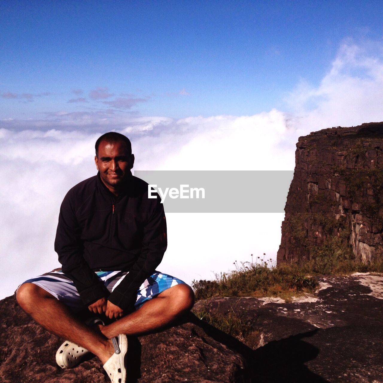 Portrait of mid adult man sitting on mt roraima against cloudy sky