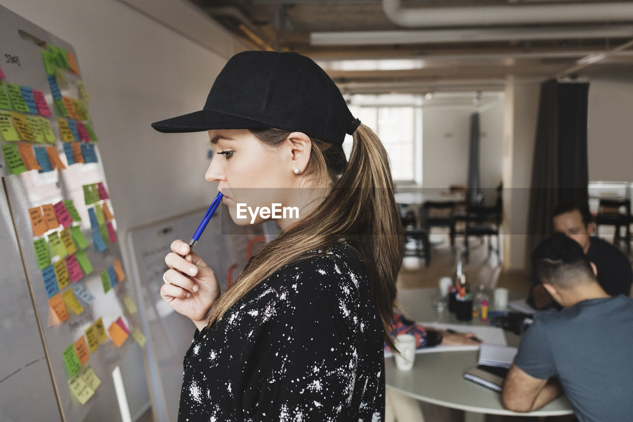 Thoughtful businesswoman standing by whiteboard with colleagues in background