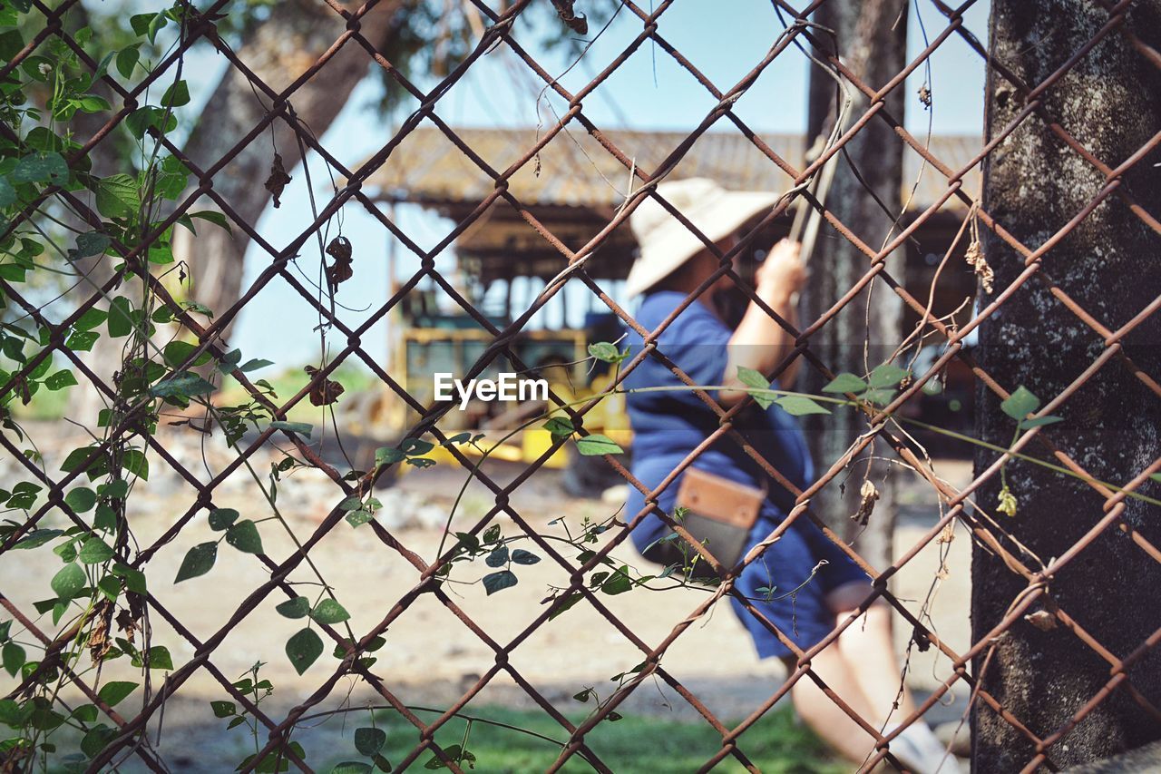 Woman sitting on swing seen through chainlink fence