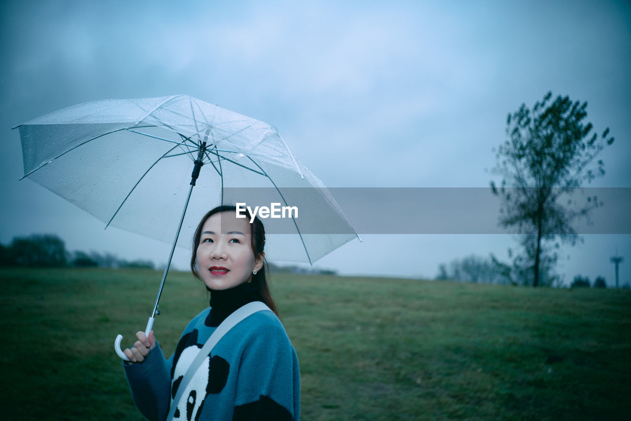 Side view of smiling woman holding umbrella on land