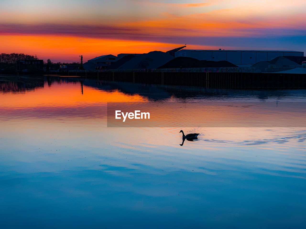 SILHOUETTE MAN IN LAKE AGAINST ORANGE SKY