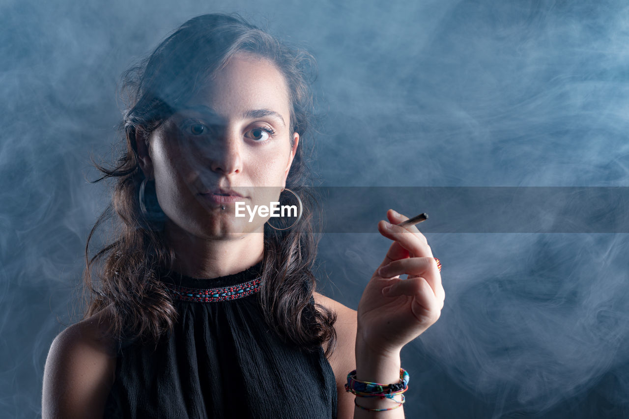 Portrait of woman smoking marijuana joint against black background