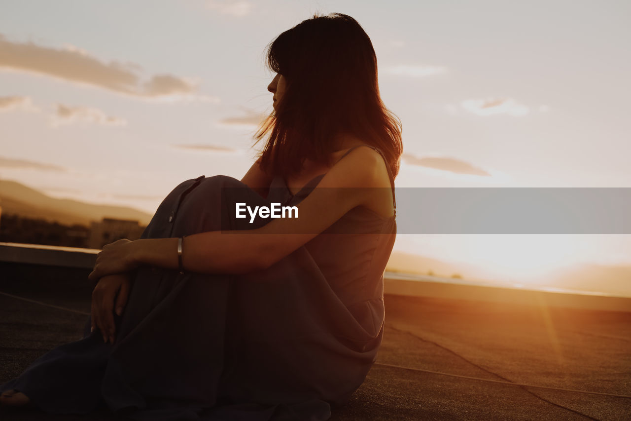 Mature woman sitting on terrace against sky during sunset