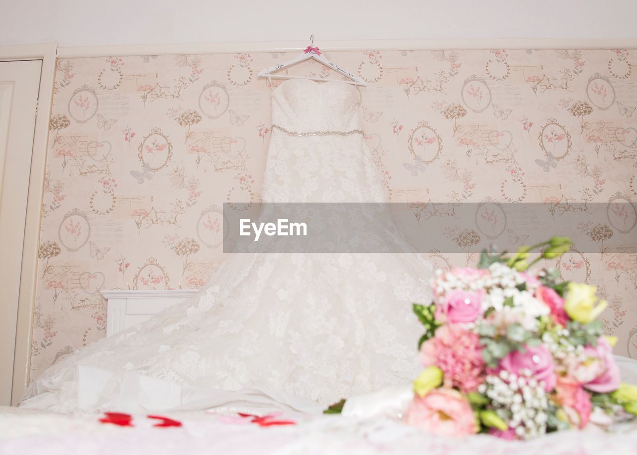 Low angle view of wedding dress hanging on bed against wall