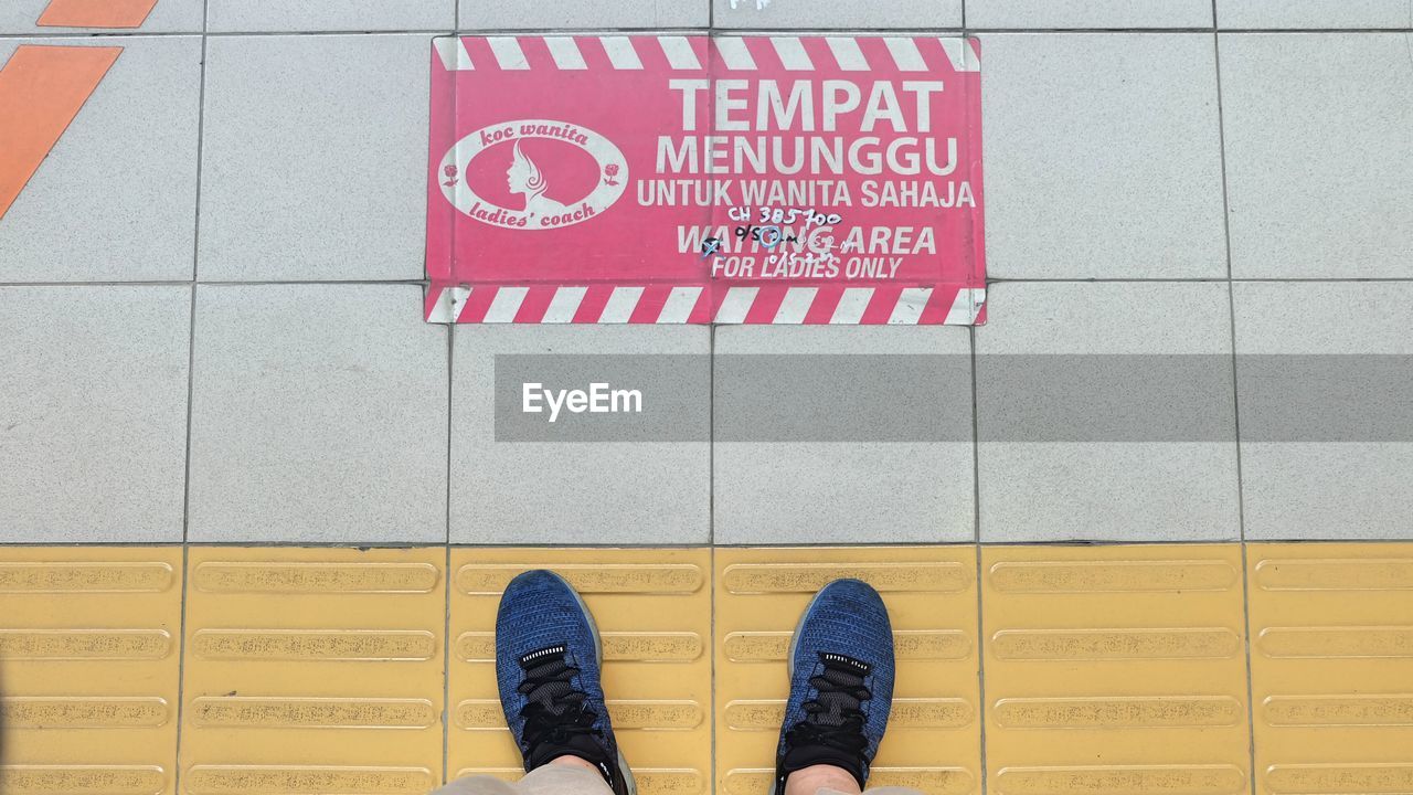 LOW SECTION OF PERSON STANDING WITH TEXT ON TILED FLOOR