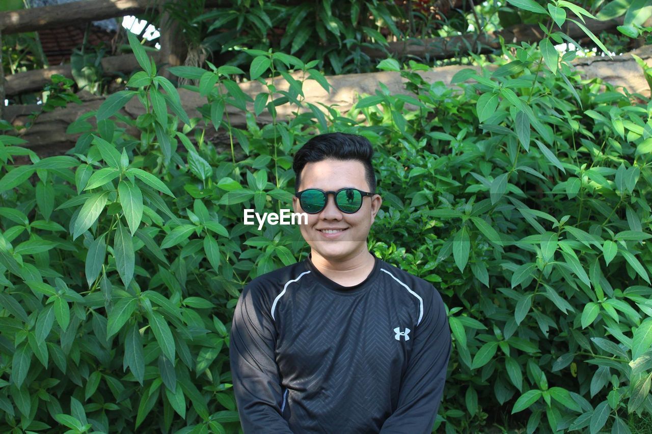 PORTRAIT OF A SMILING YOUNG MAN STANDING OUTDOORS