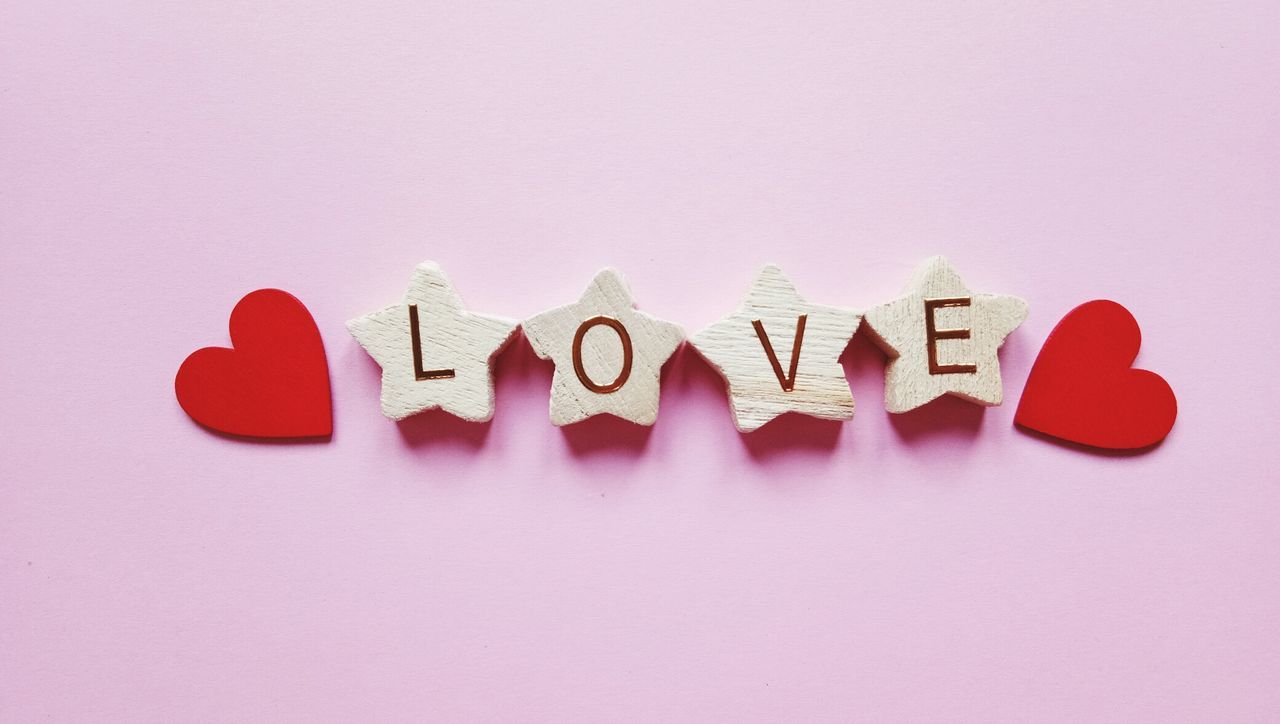 Close-up of love text and heart shape over pink background