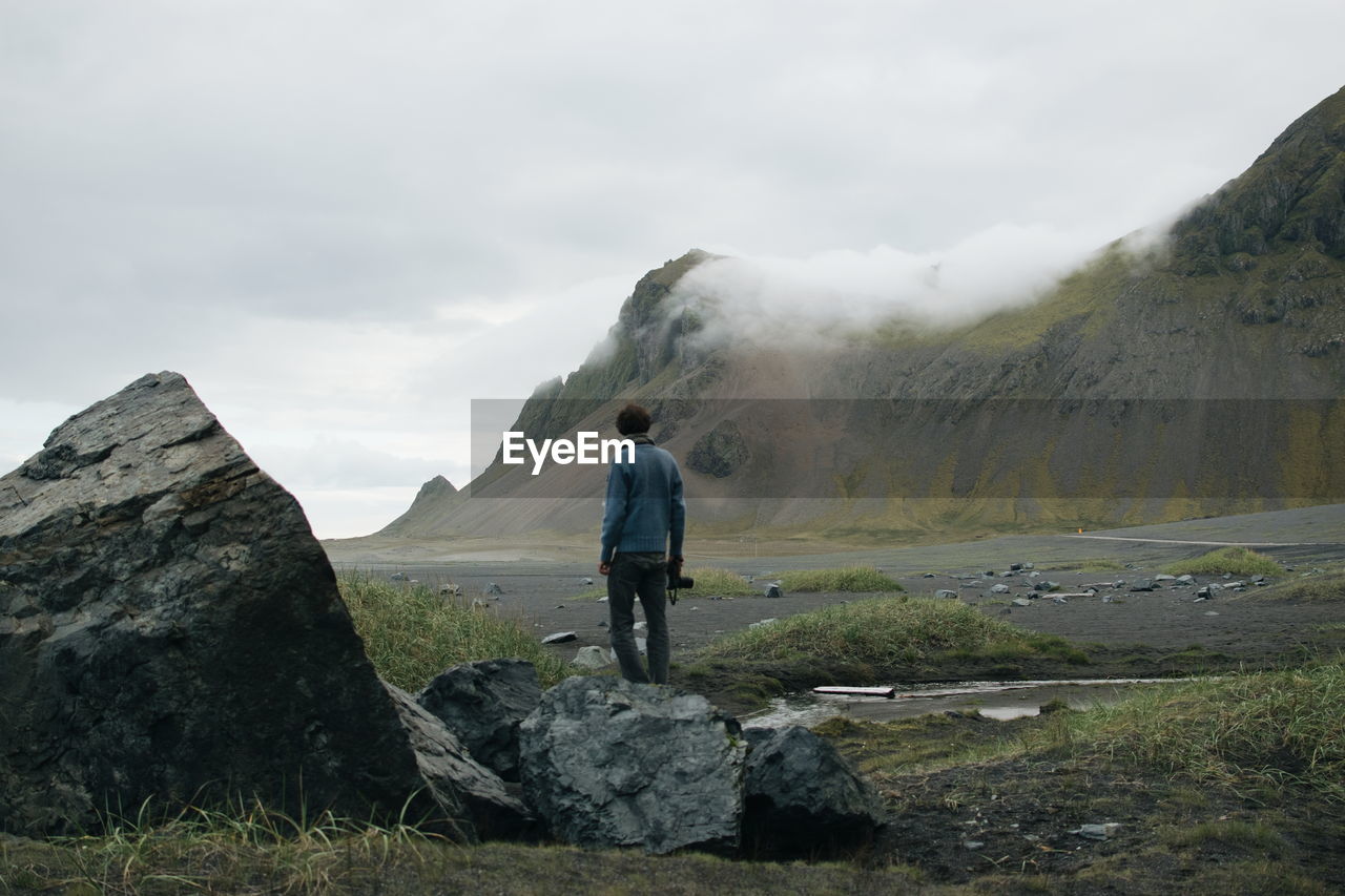 Man standing on rock against mountains during foggy weather