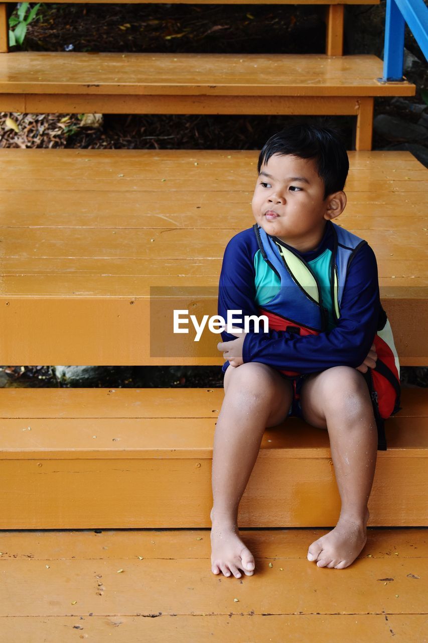 Full length of cute boy sulking while looking away on wooden steps