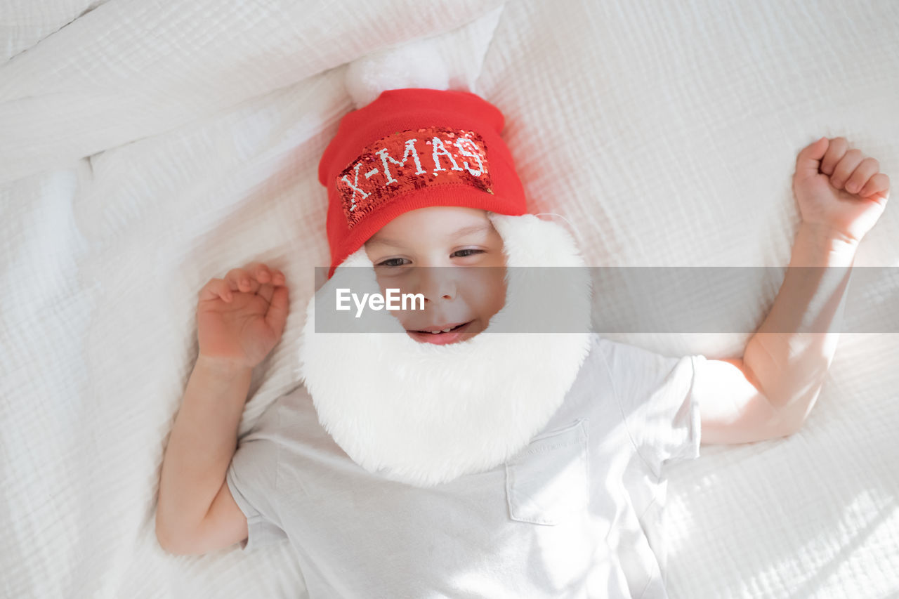 Toddler boy in santa claus costume with beard and red hat on white background